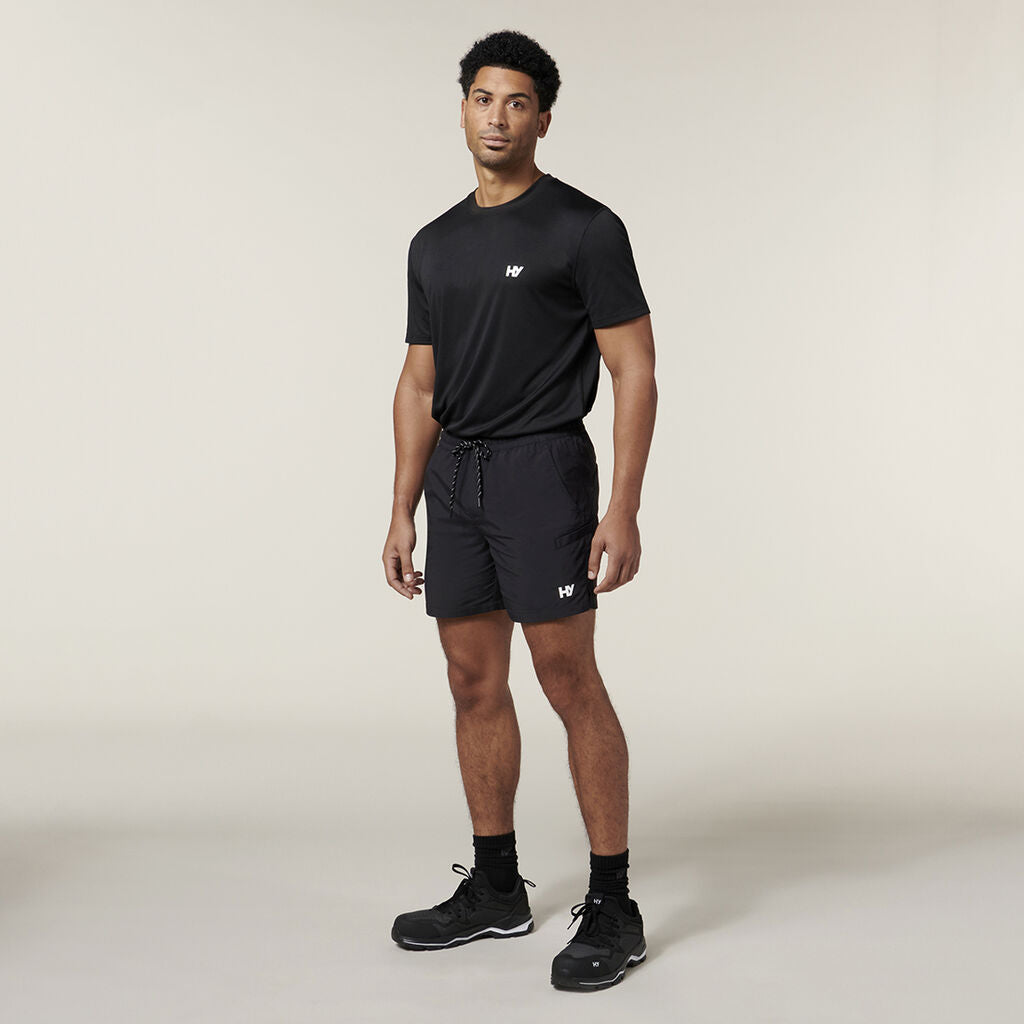 A person in a black t-shirt and shorts against a neutral background features Emz branding, completed with black socks and shoes for a sleek look.