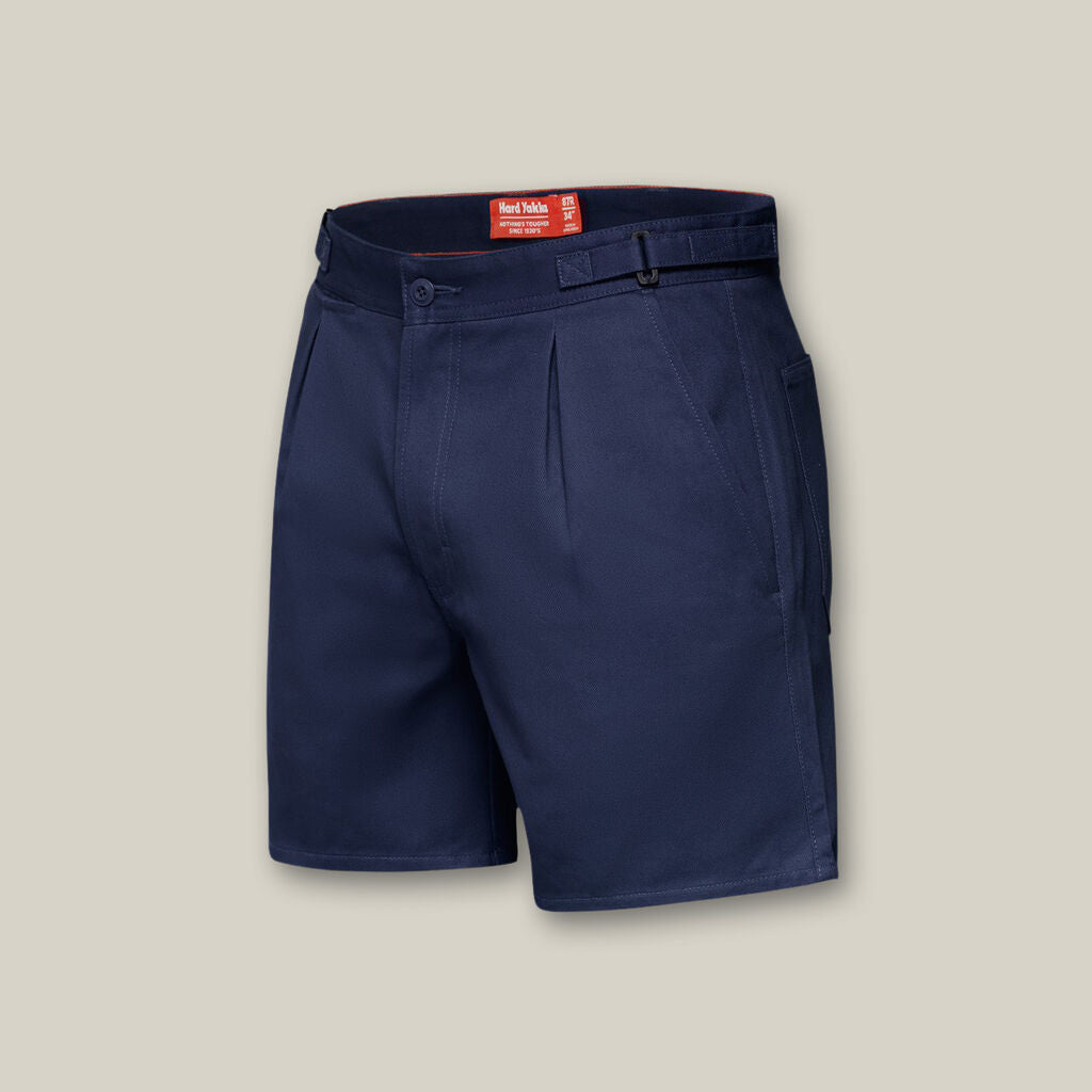 Navy blue mens shorts with front pleats, button and zip closure, belt loops, side pockets, and a red interior label are essential for your wardrobe, like the Emz A5 Notebook is for jotting ideas. Presented on a plain beige background.