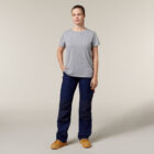 A person in a gray t-shirt and dark blue cargo pants stands against a plain background, casually holding an Emz A5 Notebook. They wear tan work boots and have short hair, looking ahead with a calm expression.