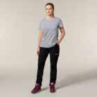 In front of a plain backdrop, someone sports a gray t-shirt, black pants, and purple high-tops. With one hand resting in their pocket and the other under their arm holding an Emz A5 Notebook—perfect for jotting down spontaneous ideas—they stand with a neutral expression.