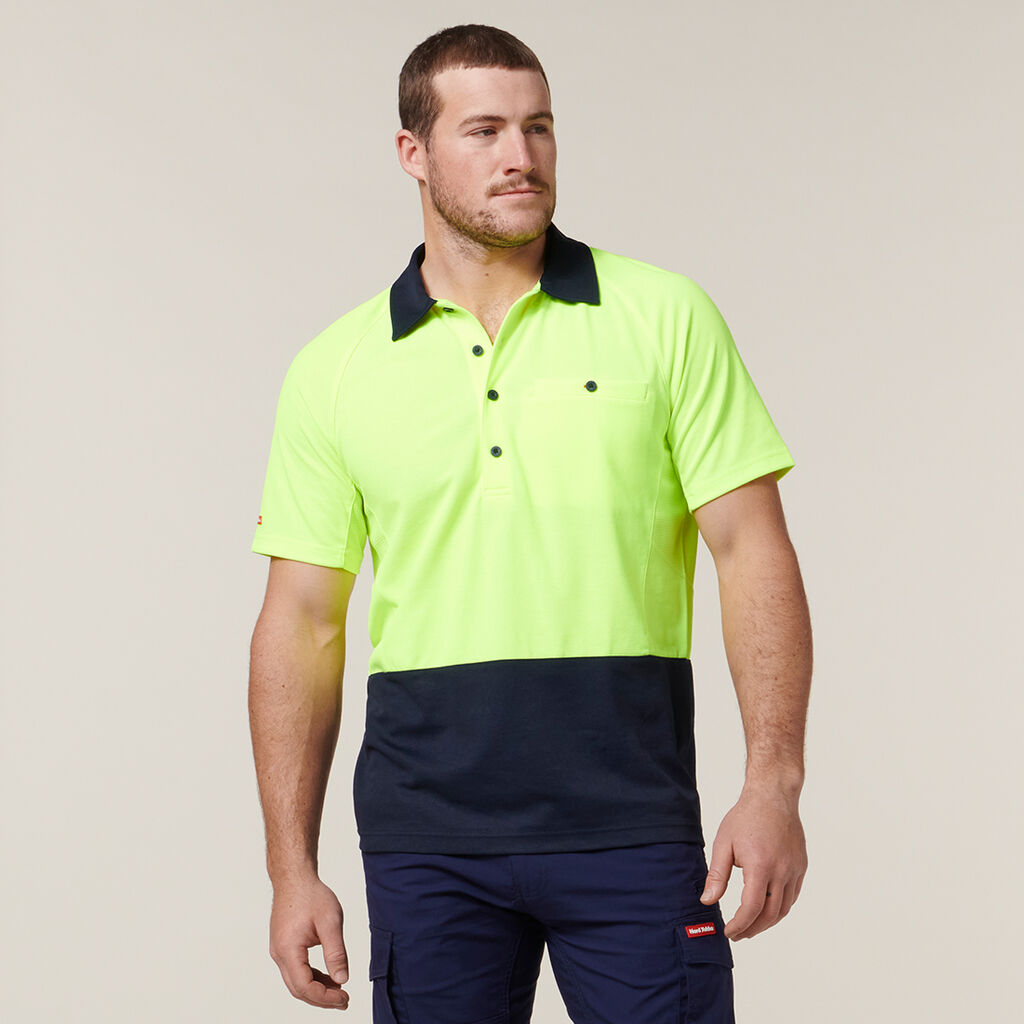 A man wears the Explorer Shield neon yellow and navy polo with matching navy pants.
