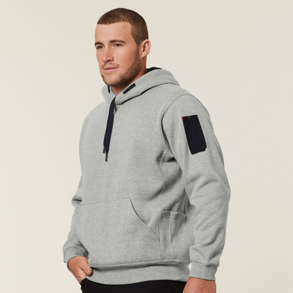 Man in Explorer Shield light gray hoodie with black sleeve patch, looking to the side.