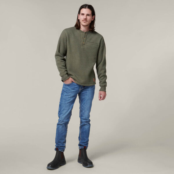 Man in green sweater, blue jeans, and Explorer Shield boots stands against a light background.