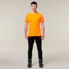 On a plain background, someone stands facing forward with arms relaxed by their sides, wearing an orange T-shirt, black pants, and black shoes—reminiscent of Emzs latest sketches in her Emz A5 Notebook.