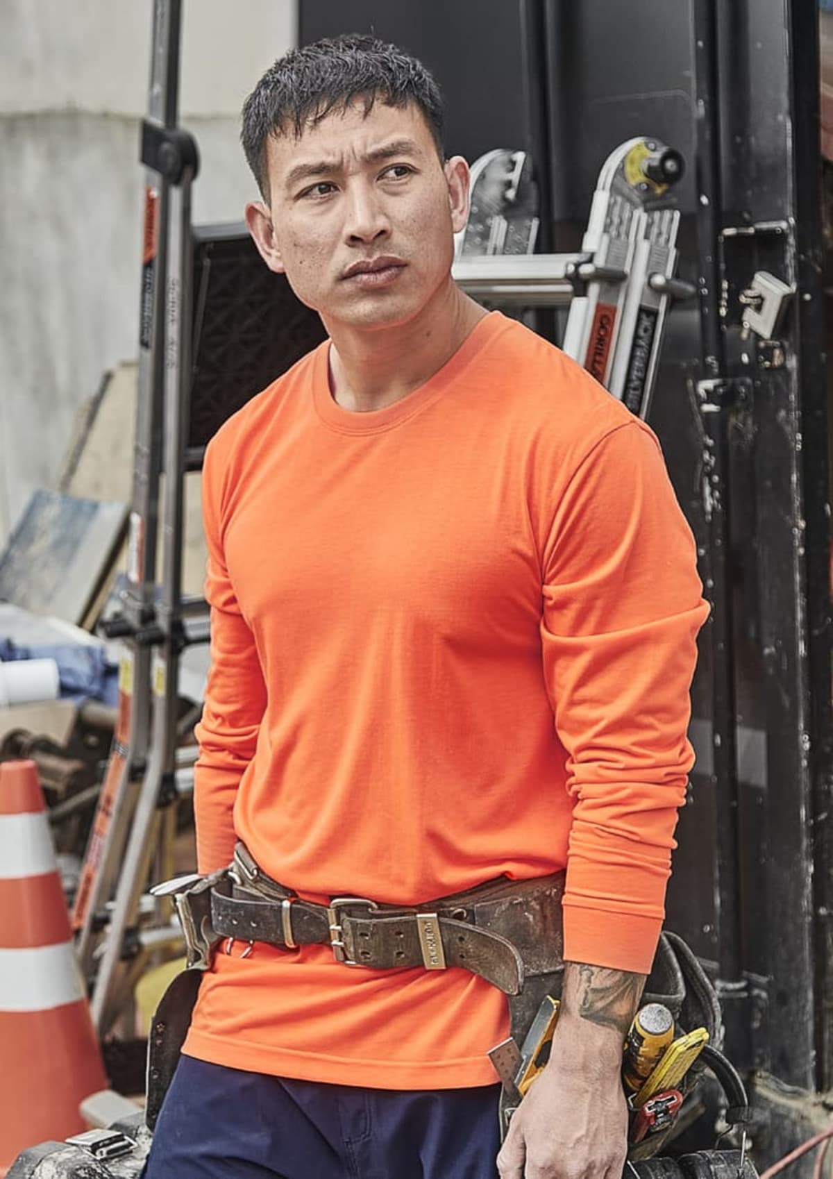 Man in orange shirt with tool belt standing at a construction site.