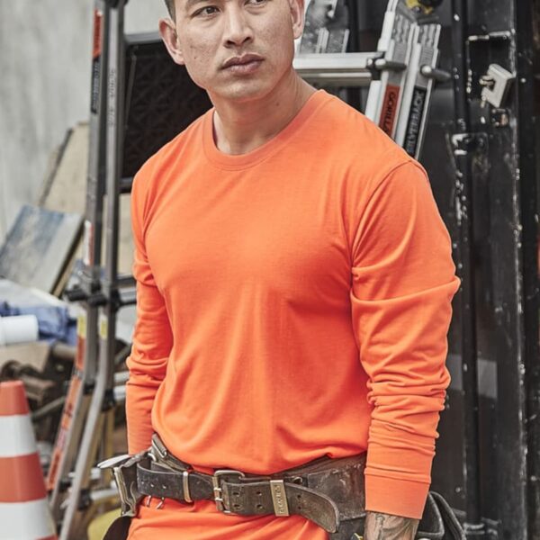 Man in orange long-sleeve shirt and tool belt stands at a construction site.