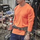 Man in orange shirt and tool belt stands at a construction site with equipment around him.