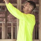 Man in a bright yellow shirt working with wires in a building under construction.