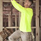 Man in a neon shirt works on wiring in a wooden-framed building under construction.