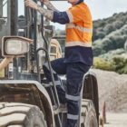 Man in safety gear climbing onto a construction vehicle at a worksite.