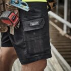 A close-up of a workers shorts with tools in a toolbelt, standing on a construction site.