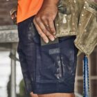 A construction worker in shorts and a tool belt holds a phone on a job site.