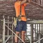 Construction worker in safety gear using a power drill on a ceiling frame indoors.