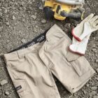 Tan work shorts, white gloves, and a circular saw on rocky ground.