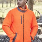 Man wearing a bright orange fleece jacket standing outdoors near trees and logs.