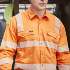 Man in orange hi-vis shirt holding a white hard hat, standing in a worksite area.