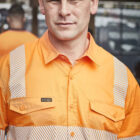 Man in orange high-visibility work shirt standing outdoors, looking at the camera.