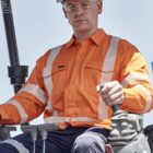 A construction worker in an orange safety shirt operates heavy machinery.
