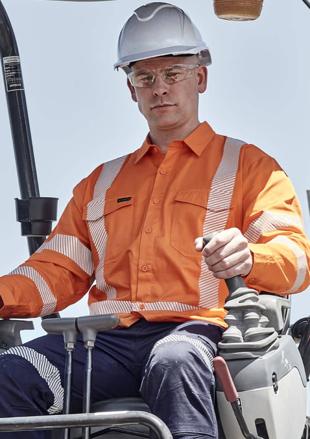 A construction worker in an orange safety shirt operates heavy machinery.