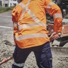 Construction worker in orange safety gear shoveling gravel at a work site.