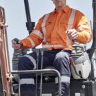 A construction worker in orange safety gear operates heavy machinery.