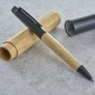 Pen with wooden barrel and gray cap on gray surface, next to open wooden case.