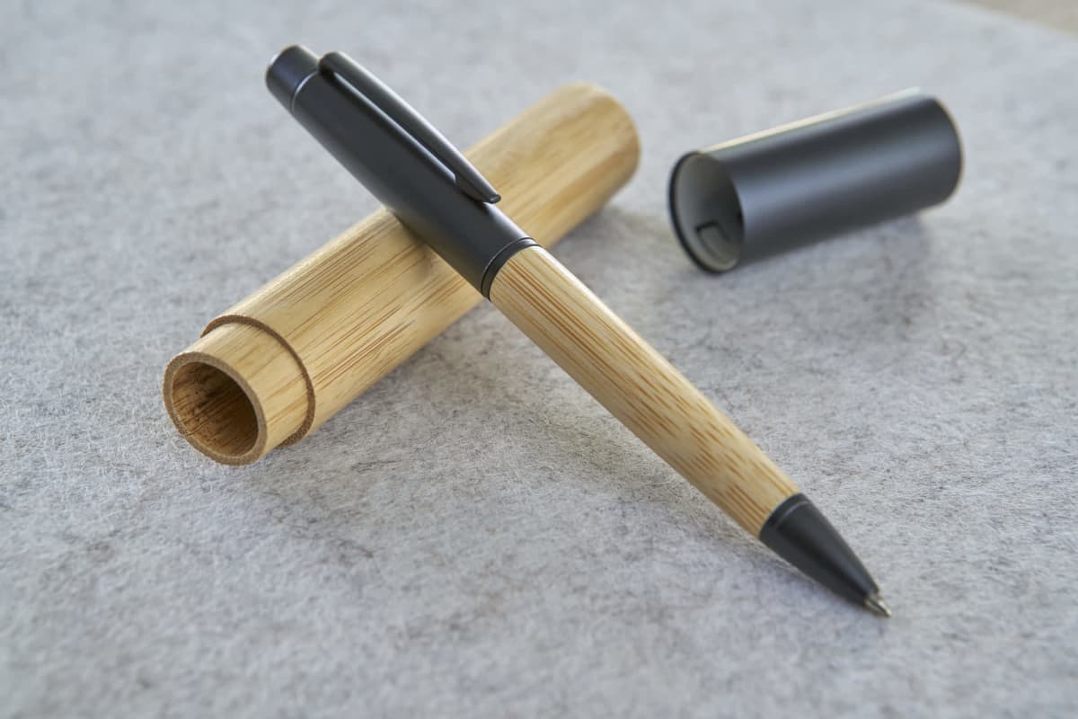 Pen with wooden barrel and gray cap on gray surface, next to open wooden case.