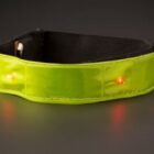 A lime green reflective dog collar with small red LED lights is displayed on a dark background. The collar is curved, indicating it might be adjustable in size.