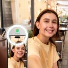 Person smiling for a selfie using a ring light attachment on a smartphone.