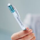 A person holds a white ergonomic pen with a translucent blue cap and a clip labeled Three Leaf Technology. The background is blurred, focusing attention on the pen.