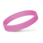 A pink silicone wristband with a smooth surface, lying on a light background. The wristband is circular and slightly tilted, casting a subtle shadow below.