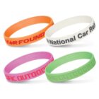 Four colorful silicone wristbands are displayed on a white background. The bands are orange, white, pink, and green, each with distinct text designs.