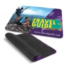 An advertisement featuring a travel-themed mouse pad. It shows a person with a backpack standing on a mountain, overlooking a scenic view. The text reads TRAVEL GUIDE and Travel made easy. The website shown is www.travelguide.com.