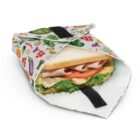 A sandwich partially wrapped in a reusable bag decorated with colorful illustrations of vegetables. The sandwich has layers of lettuce, tomato, cheese, and meat. The bag has a black Velcro closure.