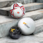 Three soccer balls on concrete steps. The top ball is white with red and blue accents labeled CROWN. The middle ball is white with a yellow star and STAR SPORTS text. The bottom ball is black with a gold eagle and BLACK EAGLE text.