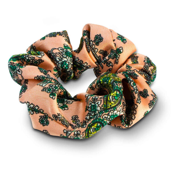 A scrunchie with intricate green floral patterns on a peach background, gathered in a circular shape.