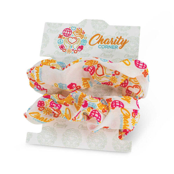 Two colorful fabric scrunchies attached to a display card labeled Charity Corner. The scrunchies have a pattern of hearts, flowers, and other playful shapes in red, yellow, and blue on a light background.
