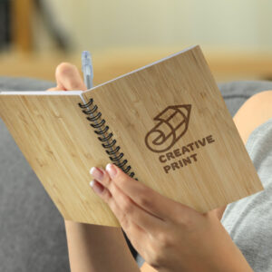 Person writing in a spiral notebook labeled Creative Print custom branded diary.