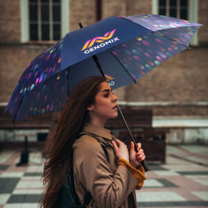 Person shields under a GENOMIX promotional umbrella in a vibrant city square.