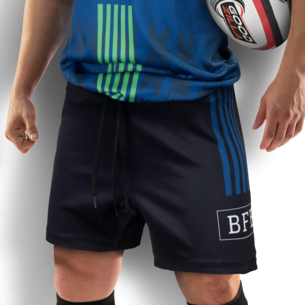 A person wearing a blue and green sports shirt and black shorts with a logo, holding a rugby ball. The image focuses on the torso and upper legs, with only the persons hands visible.