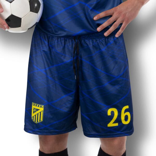 A soccer player in a blue uniform, holding a soccer ball against their hip. The shorts feature the number 26 and a yellow shield emblem. The background is a gradient from white to gray.