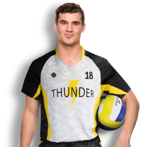 A man in a sports jersey with the number 18 and the word Thunder holds a volleyball under his arm. The jersey is gray with black and yellow accents, and features a lightning bolt design. He is smiling, standing against a white background.