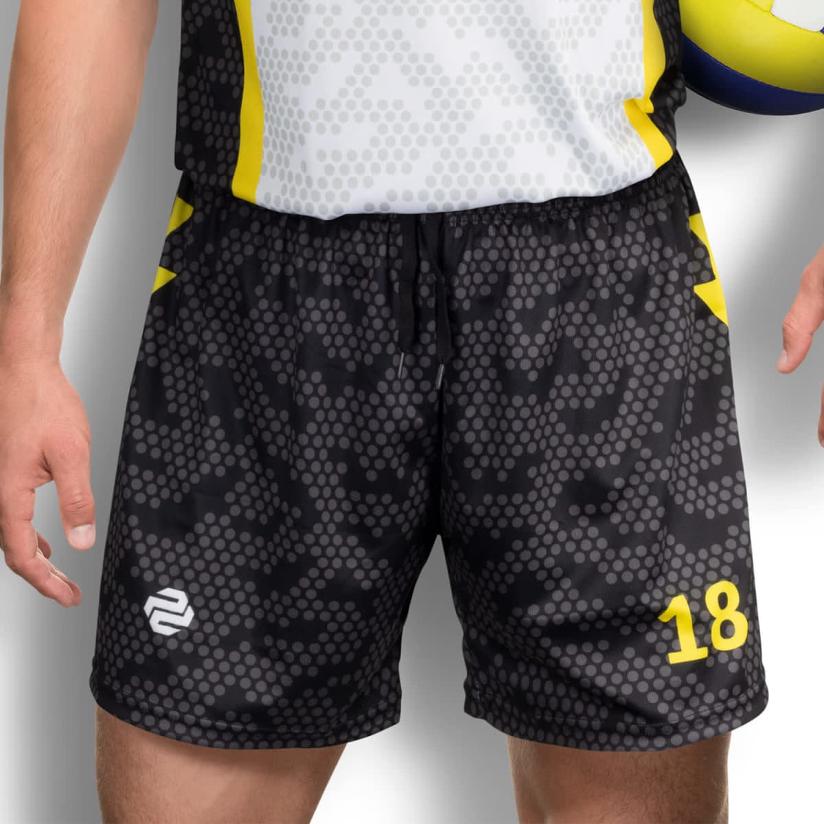 A person wearing a sports uniform with a white and gray patterned top and black shorts with yellow accents and the number 18. They are holding a volleyball under their arm.
