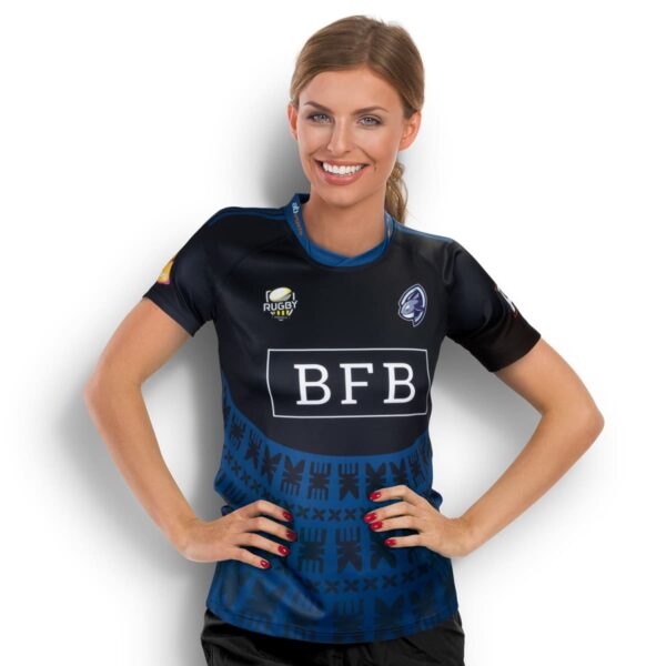 Person smiling, wearing a dark blue rugby jersey with BFB on the front. The jersey has Maori-inspired patterns and several logos, including a rugby ball. The person has hands on hips and is standing against a plain white background.