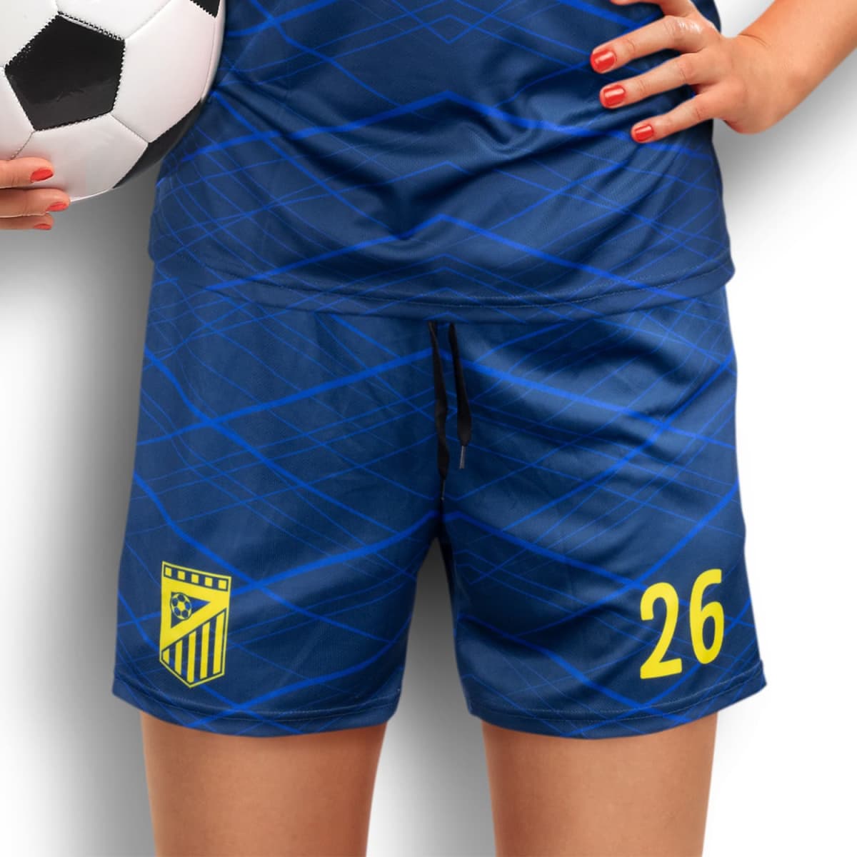 A person in a blue sports uniform with geometric patterns holds a soccer ball. The number 26 is printed in yellow on the shorts, along with an emblem. The persons fingernails are painted red.