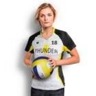 A person with short hair is wearing a black and yellow sports jersey with the number 18 and holding a volleyball. The jersey has Thunder written on it. The background is plain white.