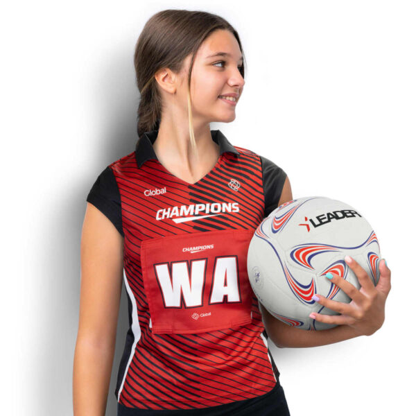 A young woman in a red and black sports jersey holding a netball. The jersey has CHAMPIONS and WA printed on it. She is looking to the side, smiling, with her hair tied back. The ball is white with red and blue patterns.