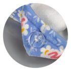 Close-up of a soft, blue fabric with white daisies and a pink pattern, featuring a clear button. The edge of the fabric is stitched, showing a textured, possibly fleece or towel-like material in white underneath.