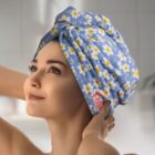 A person with a content expression looks upward, wearing a blue towel with white and yellow floral patterns wrapped around their head in a turban style. The background is softly blurred.