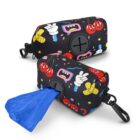 Two black dog waste bag dispensers with colorful cartoon prints, featuring cherries, bow ties, and hands. Each dispenser has a side opening for blue bags and a clip for attachment. One dispenser has a blue bag partially pulled out.